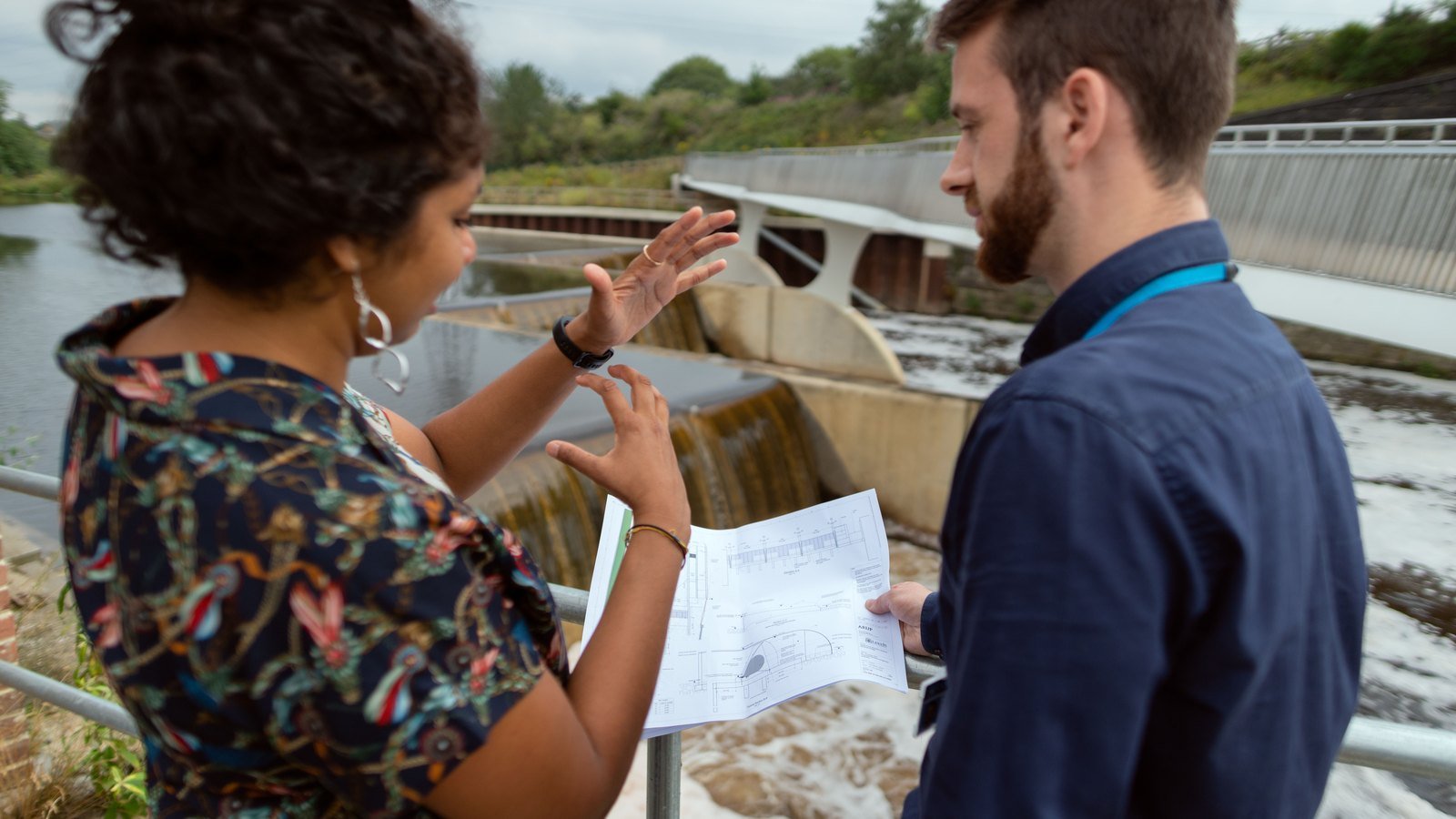 Civil engineers reviewing technical drawings beside an infrastructure project